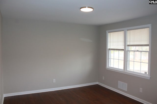 spare room featuring visible vents, baseboards, and dark wood finished floors