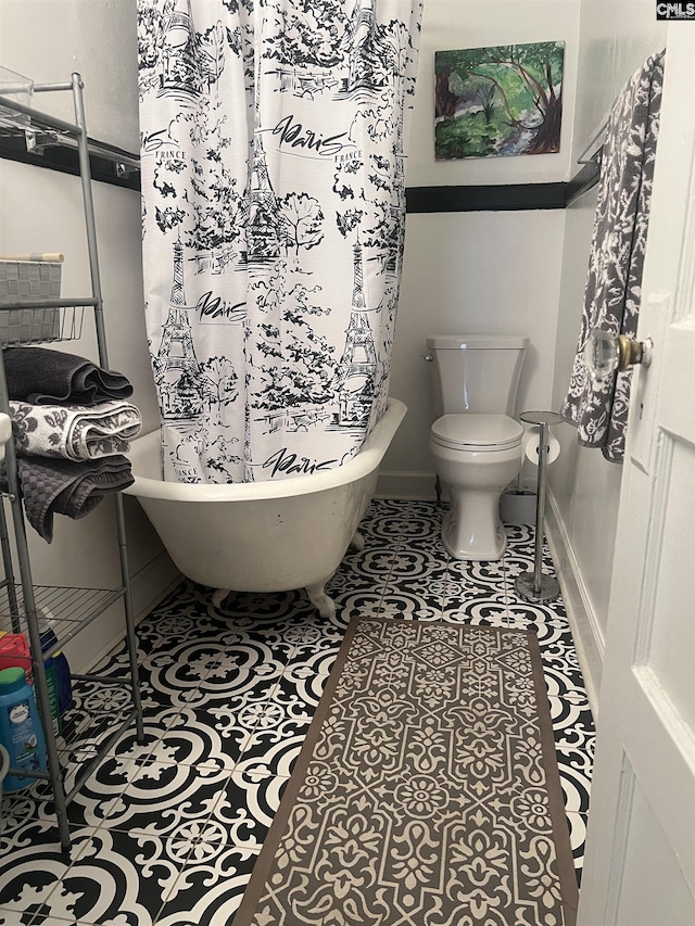 bathroom with tile patterned floors, toilet, baseboards, and a freestanding tub