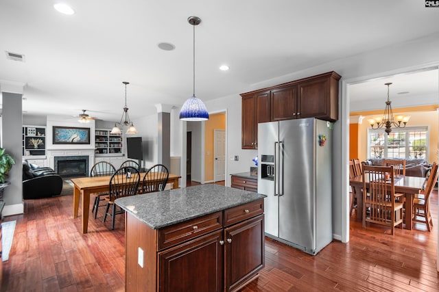 kitchen featuring visible vents, a kitchen island, dark wood finished floors, stainless steel refrigerator with ice dispenser, and a glass covered fireplace