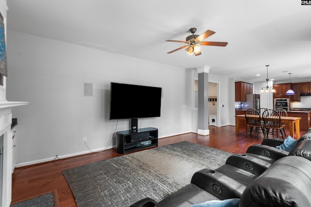 living room with baseboards, dark wood-style floors, a fireplace, and ceiling fan with notable chandelier