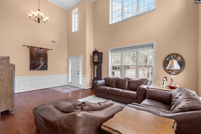 living room with a wainscoted wall, visible vents, ornamental molding, dark wood-style floors, and a chandelier