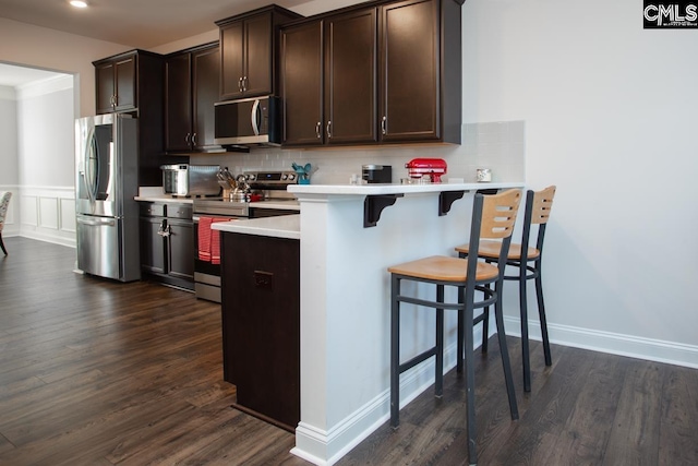 kitchen with decorative backsplash, light countertops, dark brown cabinets, appliances with stainless steel finishes, and a kitchen breakfast bar