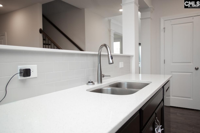 kitchen with a sink, dark wood-style floors, light countertops, decorative backsplash, and ornate columns