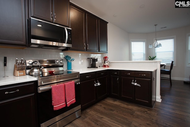 kitchen with dark wood finished floors, a peninsula, light countertops, appliances with stainless steel finishes, and tasteful backsplash