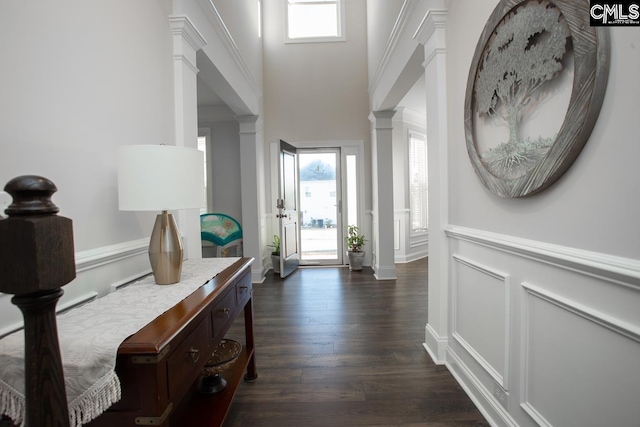 hallway with a decorative wall, dark wood finished floors, wainscoting, and ornate columns