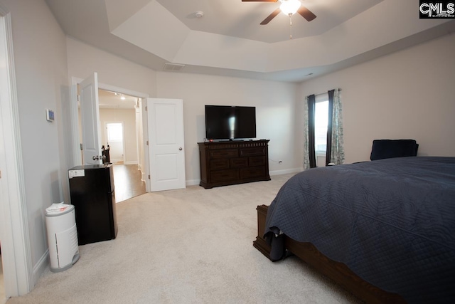 bedroom with visible vents, baseboards, light carpet, a raised ceiling, and a ceiling fan