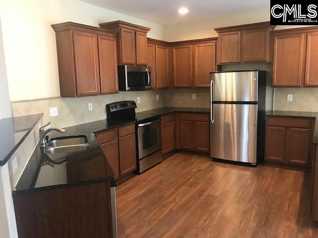 kitchen with dark wood-type flooring, a sink, dark countertops, backsplash, and stainless steel appliances