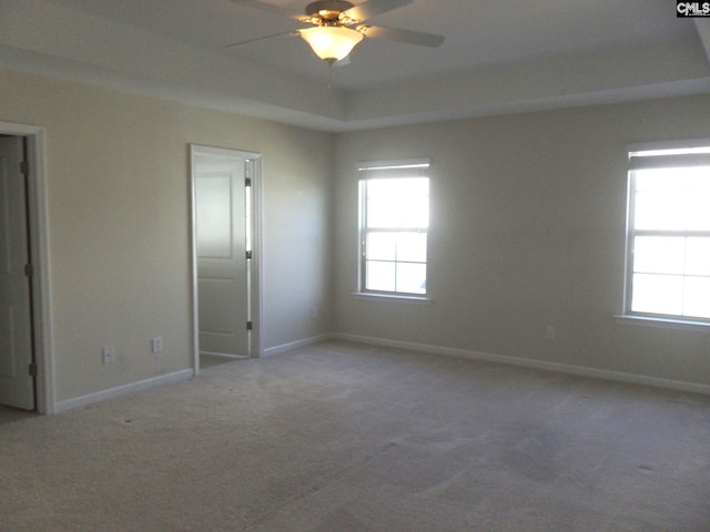 carpeted empty room featuring a tray ceiling, baseboards, and a ceiling fan