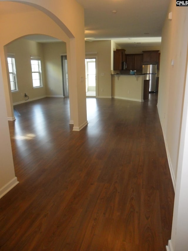 unfurnished living room featuring dark wood finished floors, arched walkways, and baseboards