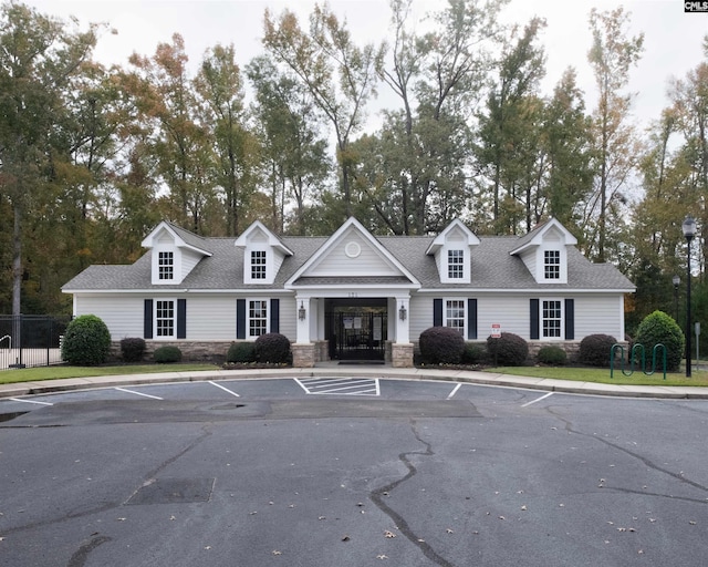 view of front of property with stone siding, roof with shingles, uncovered parking, and fence