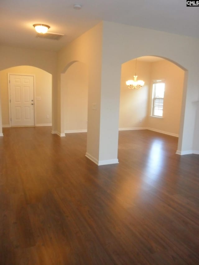 unfurnished room featuring baseboards, arched walkways, a notable chandelier, and dark wood finished floors