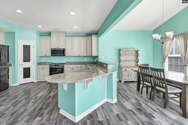 kitchen with a kitchen bar, light stone counters, a sink, stainless steel appliances, and a peninsula