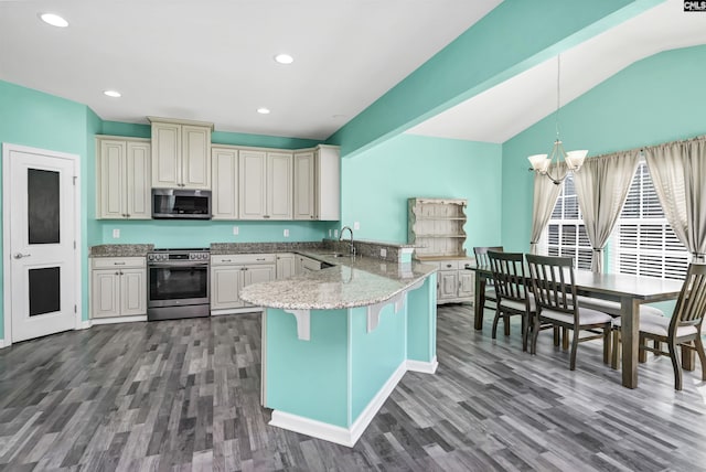 kitchen with a sink, wood finished floors, appliances with stainless steel finishes, a peninsula, and a chandelier