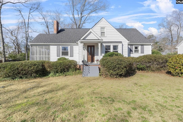 view of front of property with a chimney, a shingled roof, a front yard, and a sunroom