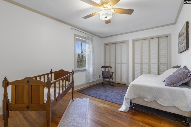 bedroom with two closets, baseboards, ornamental molding, wood finished floors, and a ceiling fan