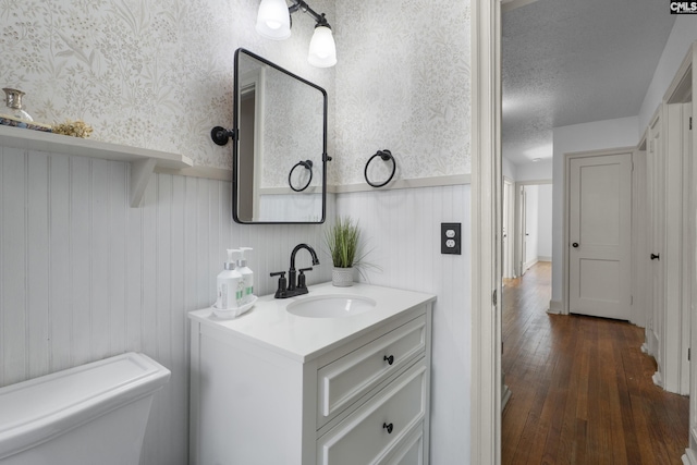 bathroom with toilet, wood-type flooring, wainscoting, wallpapered walls, and vanity