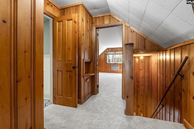 hallway with vaulted ceiling, an upstairs landing, wood walls, and carpet floors