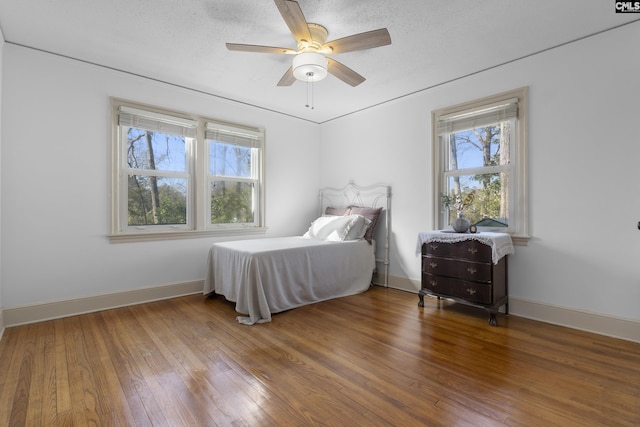 bedroom featuring a ceiling fan, baseboards, wood-type flooring, and a textured ceiling