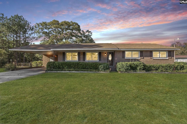 ranch-style home featuring brick siding, an attached carport, driveway, and a lawn