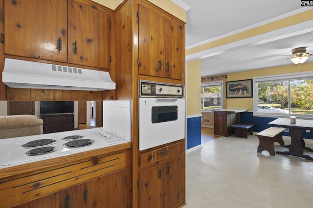 kitchen with under cabinet range hood, light floors, ornamental molding, brown cabinetry, and white appliances