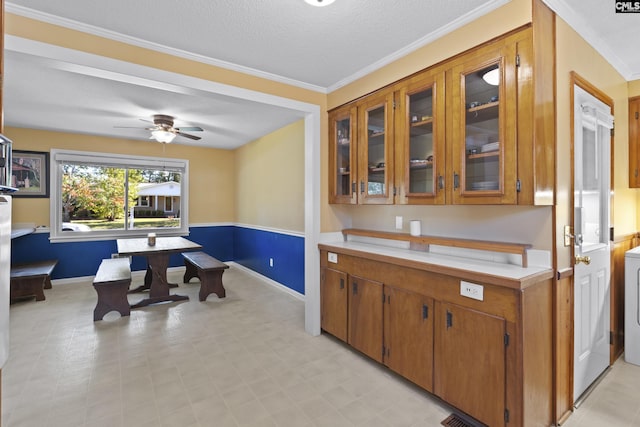 kitchen featuring glass insert cabinets, brown cabinets, ornamental molding, and light countertops