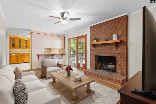 living area featuring light wood-style flooring, a ceiling fan, a textured ceiling, a fireplace, and crown molding