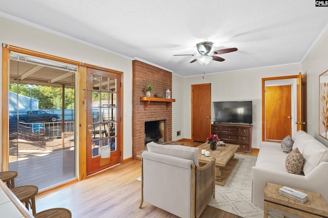 living area with ornamental molding, a ceiling fan, a textured ceiling, a fireplace, and light wood finished floors