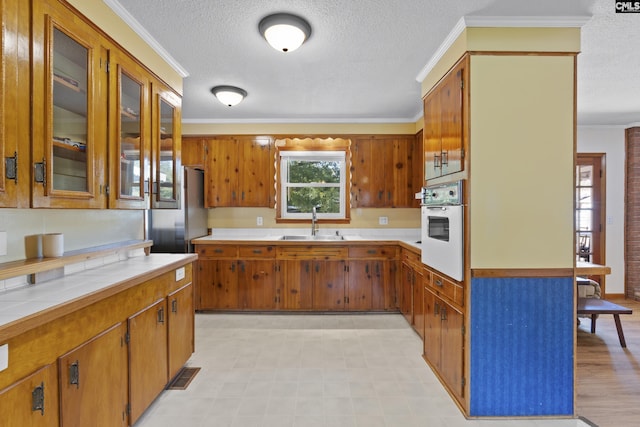 kitchen with ornamental molding, a sink, tile counters, white oven, and brown cabinets