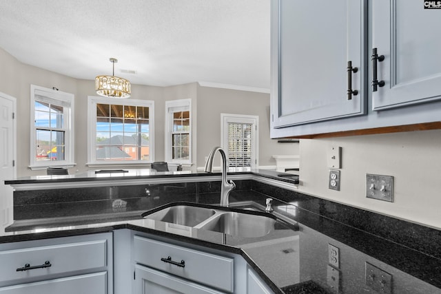 kitchen with dark stone countertops, an inviting chandelier, a sink, hanging light fixtures, and a textured ceiling