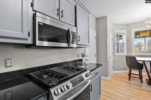 kitchen featuring gray cabinetry, a textured ceiling, appliances with stainless steel finishes, light wood finished floors, and baseboards