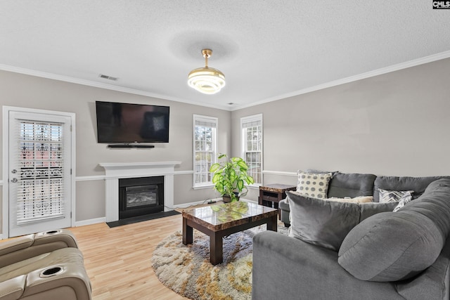 living room with visible vents, a fireplace with flush hearth, light wood-type flooring, ornamental molding, and a textured ceiling