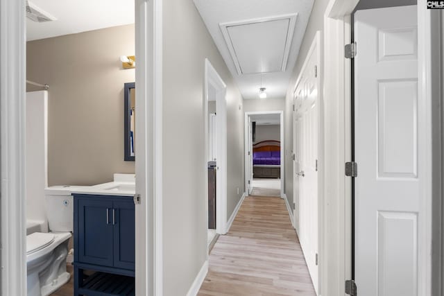 hall with attic access, baseboards, visible vents, and light wood finished floors