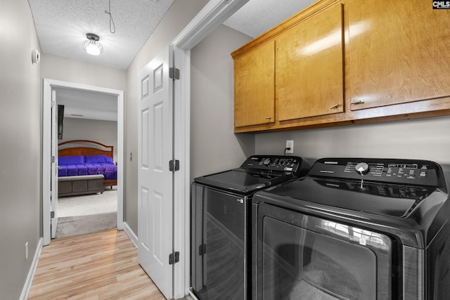 clothes washing area featuring washer and clothes dryer, cabinet space, light wood finished floors, and a textured ceiling