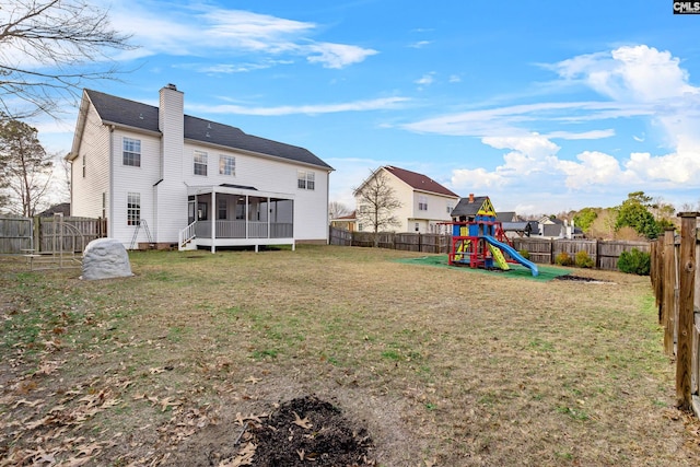 rear view of property featuring a lawn, a fenced backyard, a playground, a sunroom, and a chimney