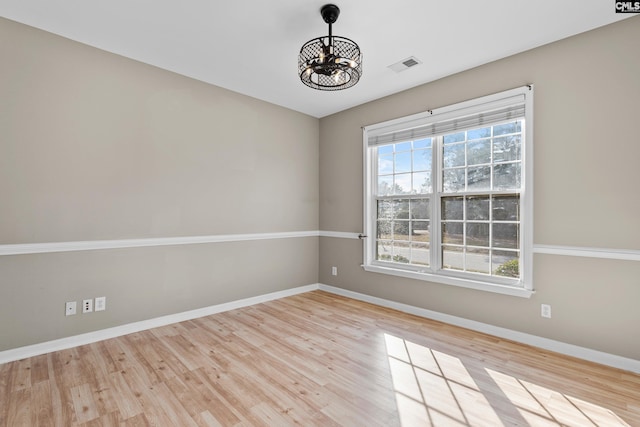 spare room with a notable chandelier, visible vents, baseboards, and wood finished floors