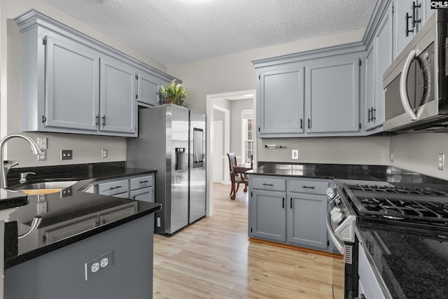 kitchen with light wood finished floors, dark stone countertops, stainless steel appliances, a textured ceiling, and a sink