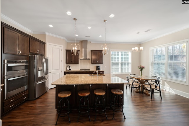 kitchen with a sink, stainless steel appliances, dark brown cabinetry, wall chimney range hood, and light stone countertops