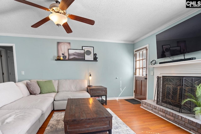 living area featuring baseboards, ornamental molding, a fireplace, wood finished floors, and a textured ceiling