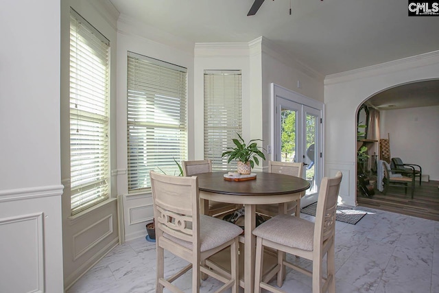 dining space with ornamental molding, wainscoting, arched walkways, a decorative wall, and marble finish floor