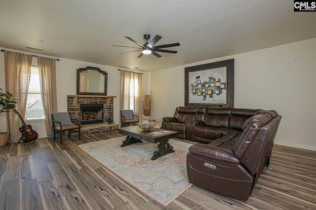 living area featuring a stone fireplace, baseboards, a ceiling fan, and wood finished floors