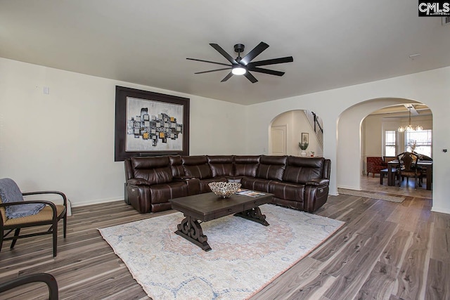 living area featuring arched walkways, ceiling fan with notable chandelier, baseboards, and wood finished floors