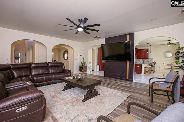 living room with arched walkways, visible vents, dark wood-type flooring, and a ceiling fan