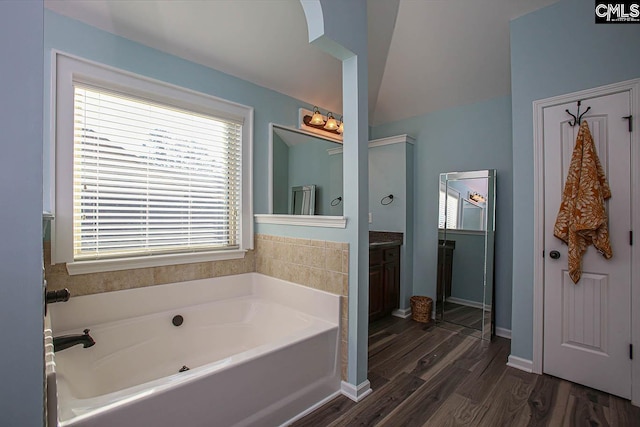 bathroom featuring baseboards, wood finished floors, a bath, and vanity