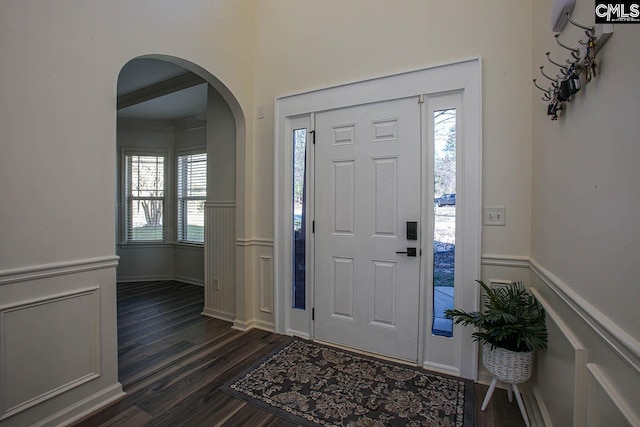 foyer featuring dark wood finished floors, a wainscoted wall, plenty of natural light, and arched walkways