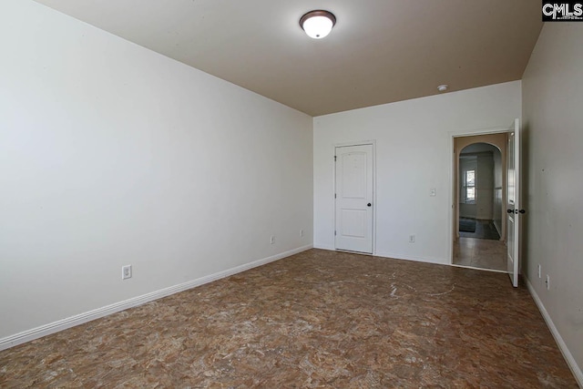 empty room featuring baseboards and arched walkways