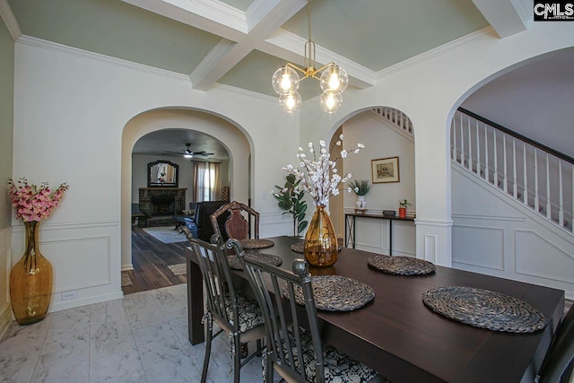 dining room featuring a fireplace with raised hearth, stairs, beam ceiling, a decorative wall, and coffered ceiling