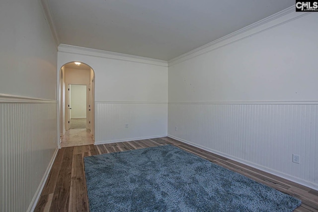 spare room featuring arched walkways, a wainscoted wall, ornamental molding, and wood finished floors