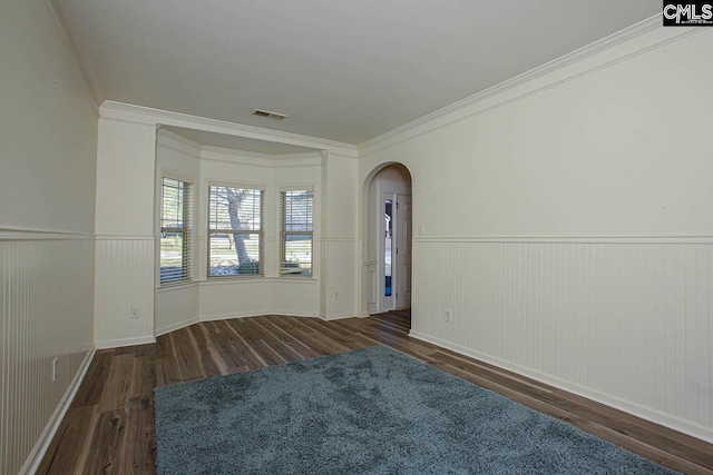 spare room featuring wood finished floors, visible vents, arched walkways, and wainscoting