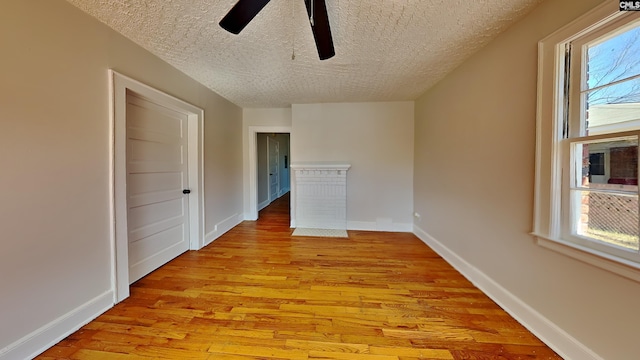 unfurnished room with a ceiling fan, baseboards, light wood finished floors, and a textured ceiling