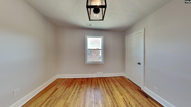 spare room with baseboards, visible vents, wood-type flooring, and a textured ceiling